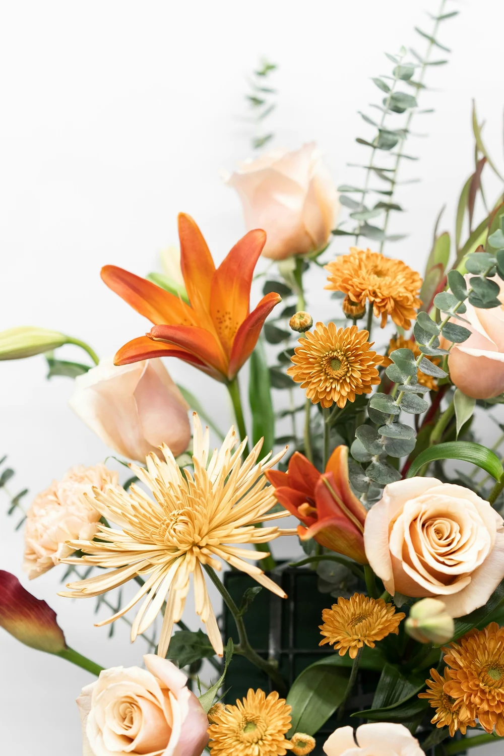 Close view of orange lily petals, cream roses, golden flowers and eucalyptus leaves.
