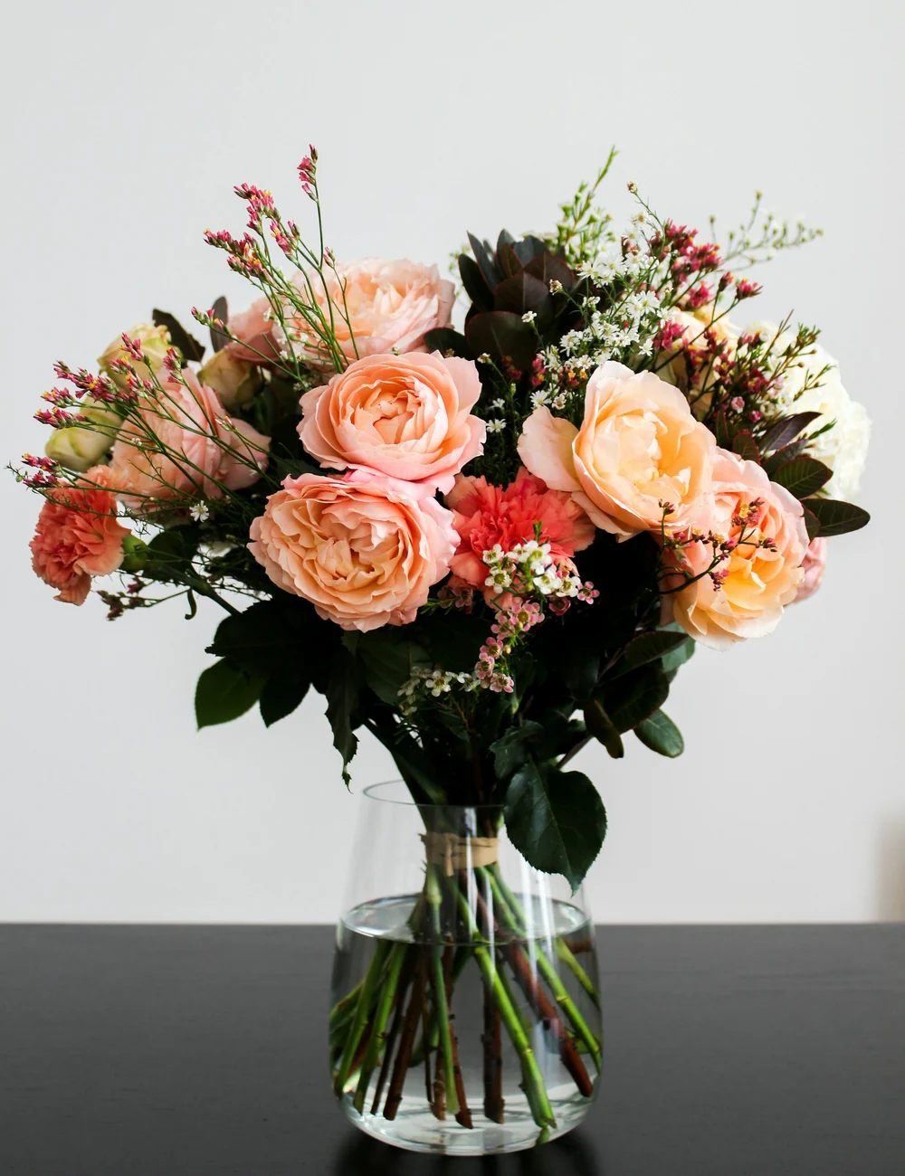 The peach and cream bouquet in a clear glass vase against a pale gray wall.